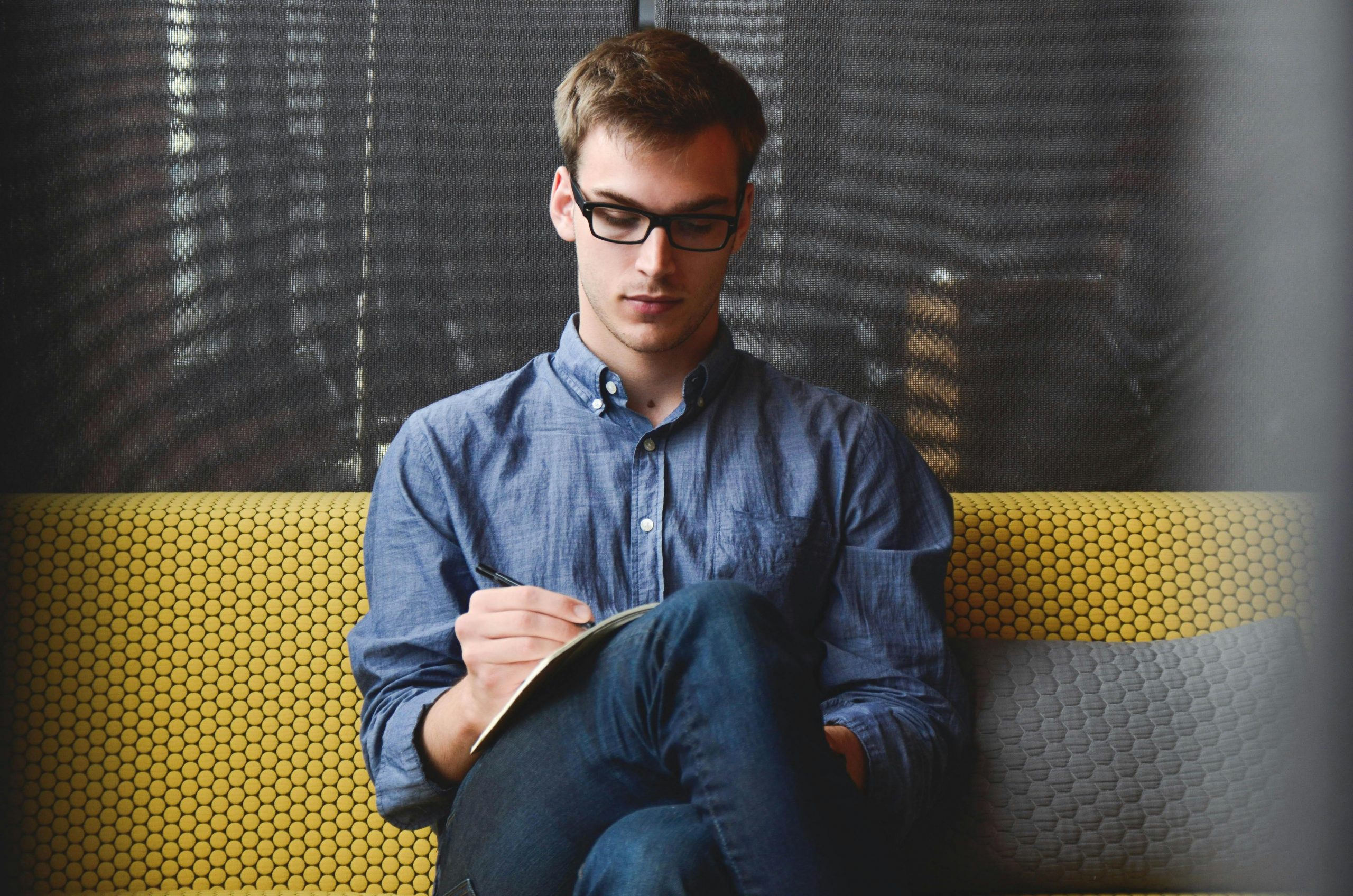 serious-looking man sitting cross-legged, writing in a notebook on his lap